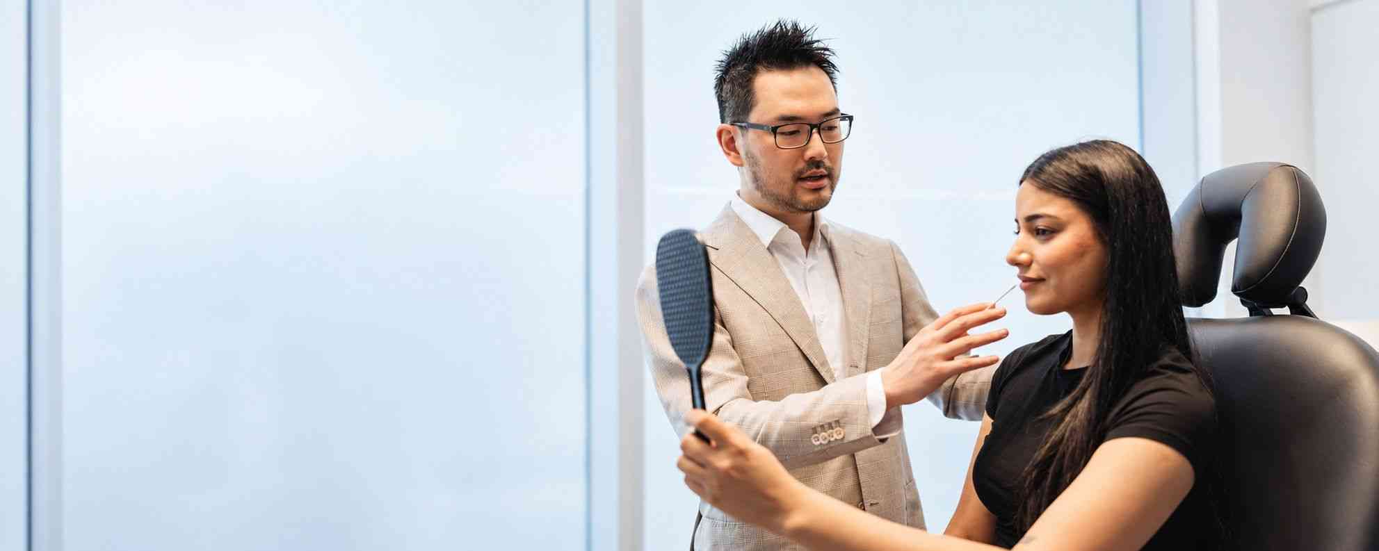 Dr. Danny Guo assessing facial balance with a patient holding a mirror in Calgary