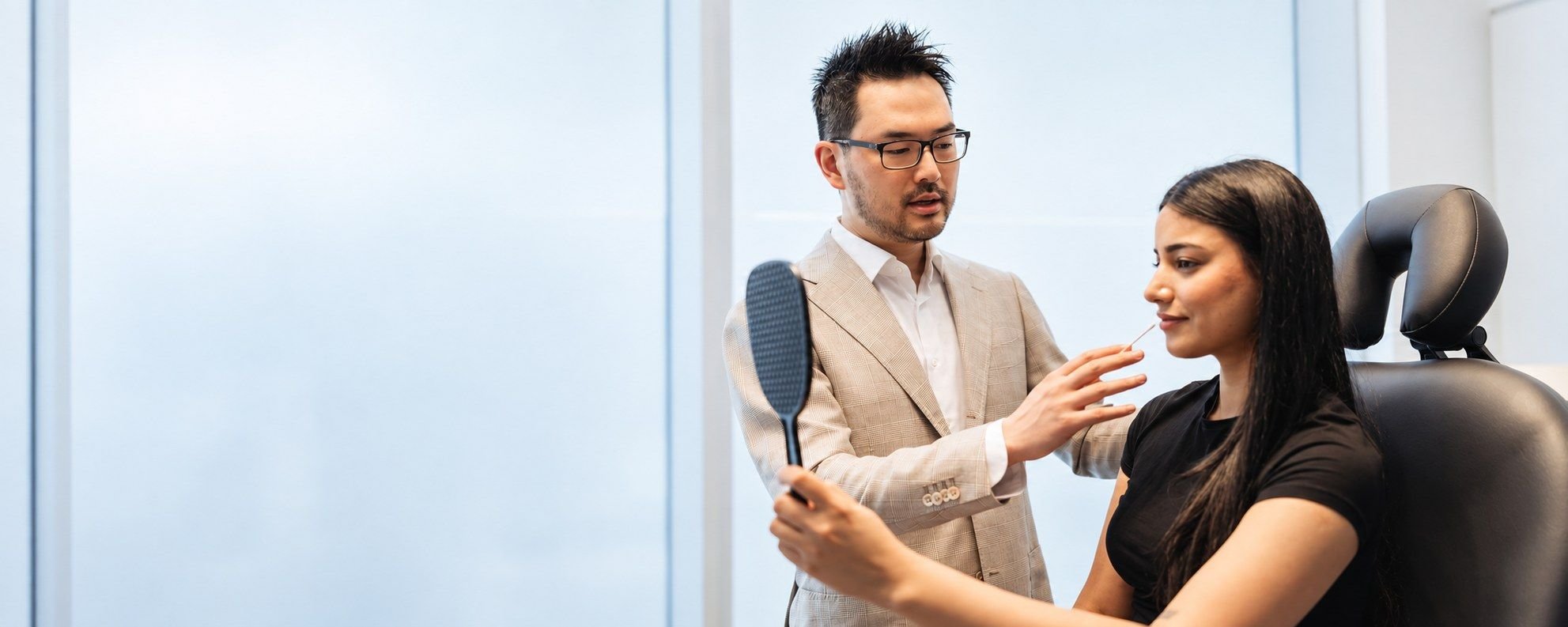 Dr. Danny Guo assessing facial balance with a patient holding a mirror in Calgary